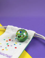 Laden Sie das Bild in den Galerie-Viewer, Ava & Yves Supermurmel Grün – Muranoglas-Murmel (25 mm) mit bunten Konfetti-Steinchen im bestickten Stoffbeutel.