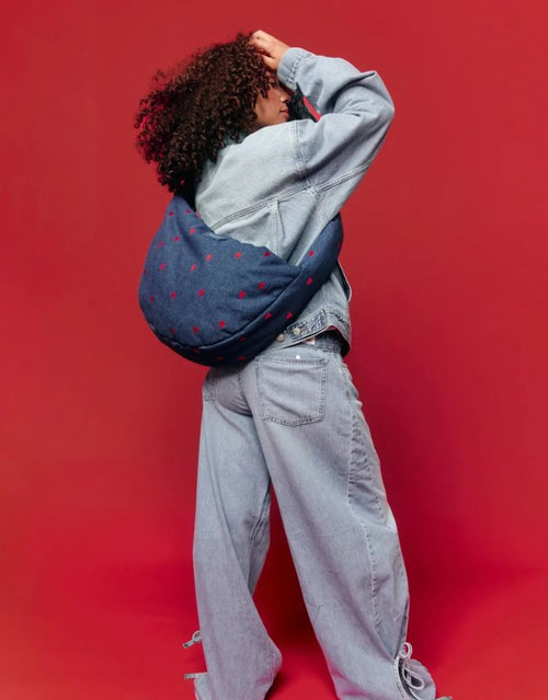 Studio Noos Cross Body Umhängetasche aus dunkelblauem gepolstertem Denim mit gestickten roten Herzen und Platz für einen 13-Zoll-Laptop getragen.