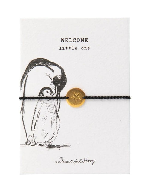 Schmuck-Postkarte Pinguin von A Beautiful Story mit „welcome little one“-Motiv und schwarzem Armband mit goldfarbenem Sternanhänger.