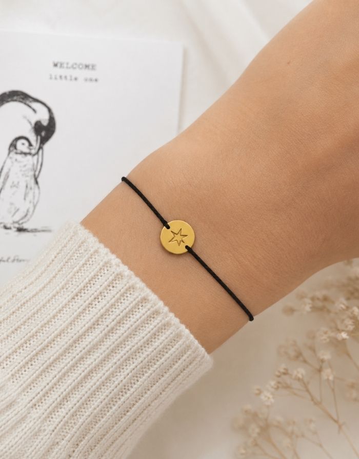 Schmuck-Postkarte Pinguin von A Beautiful Story mit „welcome little one“-Motiv und schwarzem Armband mit goldfarbenem Sternanhänger, getragen.