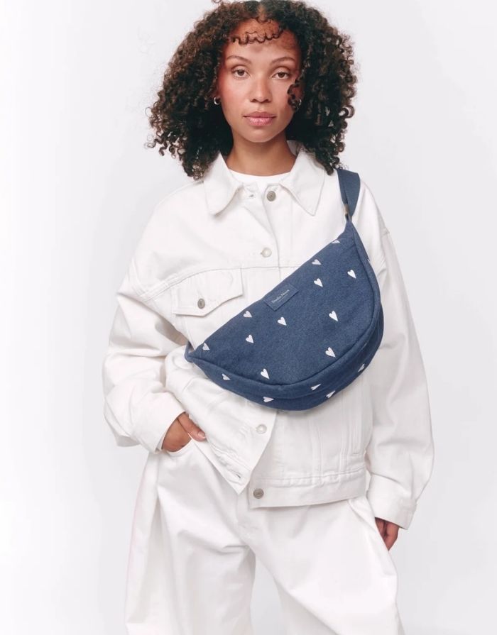 Studio Noos Fanny Pack Denim Blue White Hearts aus dunkelblauem gepolstertem Denim mit gestickten weißen Herzen und verstellbarem Trageriemen am Model.