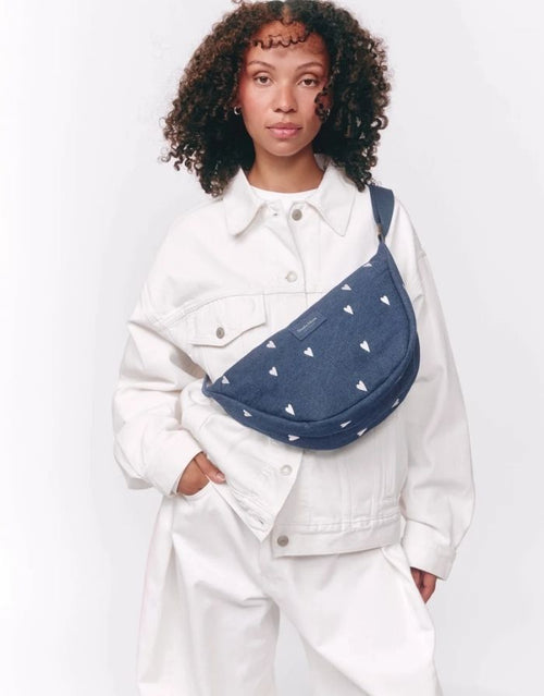 Studio Noos Fanny Pack Denim Blue White Hearts aus dunkelblauem gepolstertem Denim mit gestickten weißen Herzen und verstellbarem Trageriemen am Model.