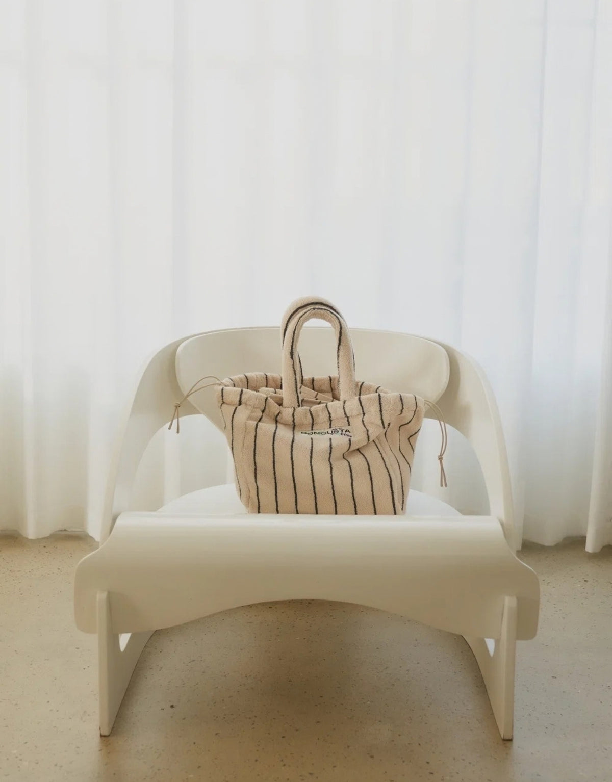  Frottee Handtasche von Bongusta in Creme und Ink aus 100 % Bio-Baumwolle mit Streifenmuster und verstellbarem Nylon-Kordelzug auf einem Stuhl