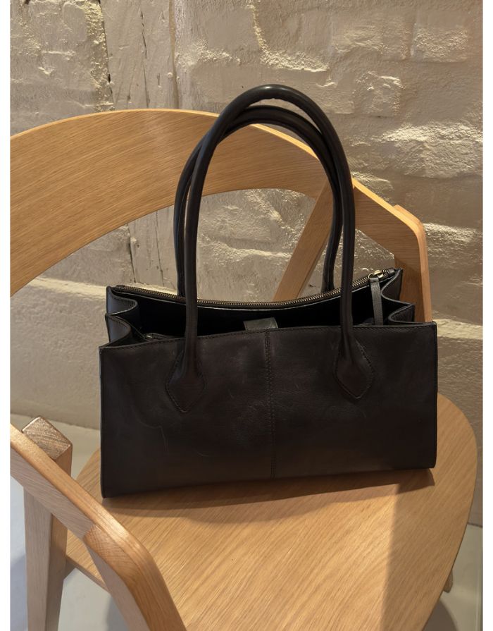 Schwarze Ora Small Ledertasche von Re:Designed mit vier Innenfächern, Druckknopfverschluss und handgefertigtem Design Auf Stuhl