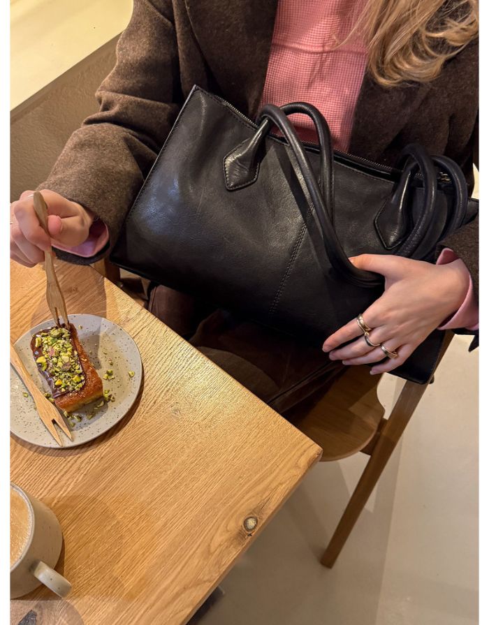 Schwarze Ora Small Ledertasche von Re:Designed mit vier Innenfächern, Druckknopfverschluss und handgefertigtem Design Auf Schoß von Model