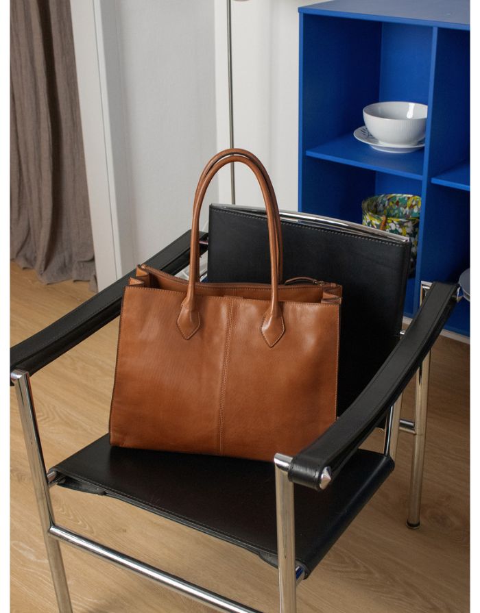  Braune Ora Big Ledertasche von Re:Designed mit großem Hauptfach, praktischen Innenfächern und handgefertigtem Design auf Stuhl
