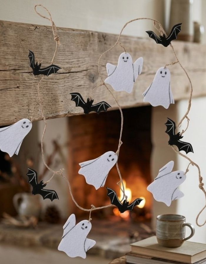 Halloween Girlande Ghostie von BOLTZE in Schwarz und Weiß mit Gespenstern und Fledermäusen, 160 cm lang, vor einem Kamin.