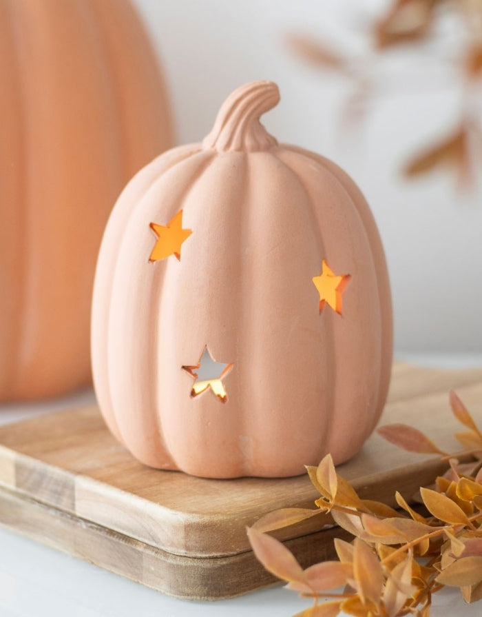 Terrakotta Kürbis-Teelichthalter von Something Different mit ausgestanzten Sternen für eine stimmungsvolle Herbst- und Halloween-Dekoration auf Holzbrett
