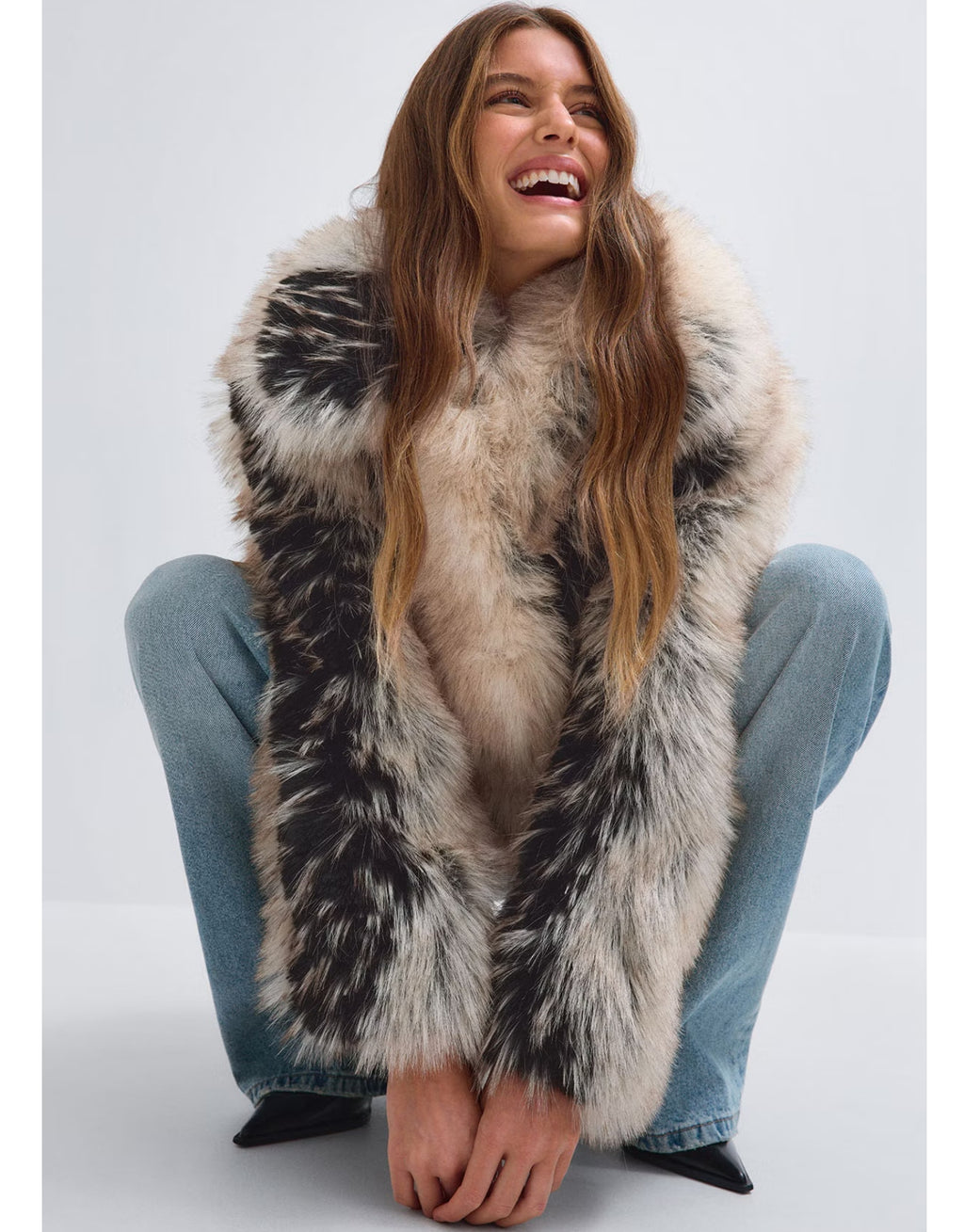 Cremeweiß-schwarze Faux Fur Short Jacke von Gina Tricot mit flauschigem Kunstfell, breitem Kragen, Knopfverschluss und kurzer Oversize-Silhouette am Model im Sitzen
