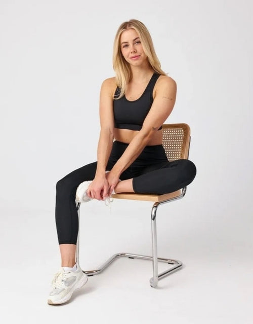 High-Waist-Leggings von SNOCKS mit hohem Bund aus flexiblem, blickdichtem Material mit recyceltem Polyester am Model auf einem Stuhl