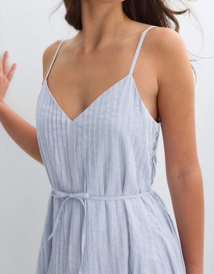 Gina Tricot Pleated Dress in Hellblau als plissiertes Maxikleid mit V-Ausschnitt und schmalen Trägern an Model von vorne im Detail
