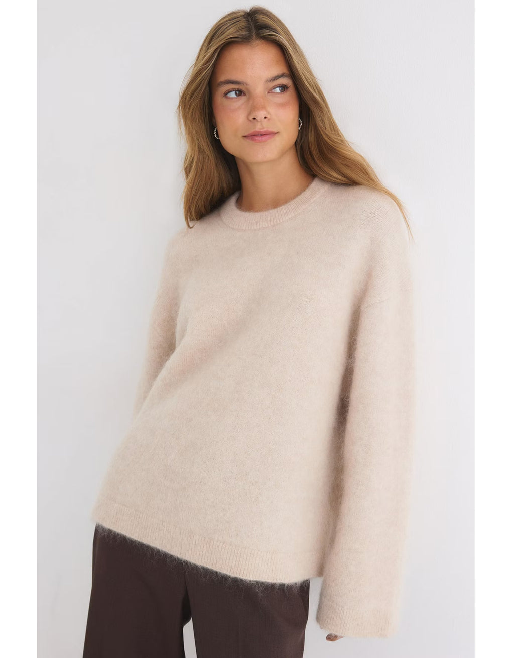 Beiger Mohair Pullover von Gina Tricot mit feiner, flauschiger Strickstruktur, lockerer Passform, langen Ärmeln und klassischem Rundhalsausschnitt am Model von vorne