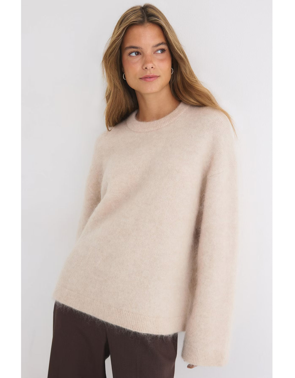 Beiger Mohair Pullover von Gina Tricot mit feiner, flauschiger Strickstruktur, lockerer Passform, langen Ärmeln und klassischem Rundhalsausschnitt am Model von vorne