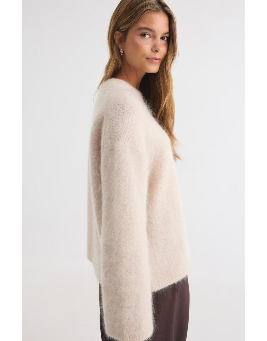  Beiger Mohair Pullover von Gina Tricot mit feiner, flauschiger Strickstruktur, lockerer Passform, langen Ärmeln und klassischem Rundhalsausschnitt am Model von der Seite