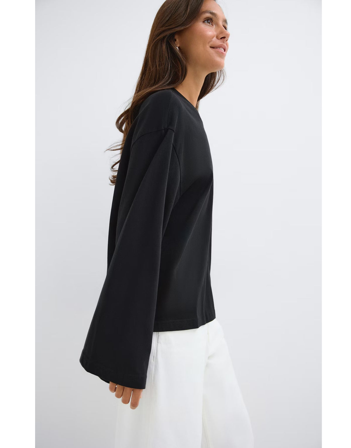 Schwarzes Loose Fit Long Sleeve Shirt von Gina Tricot mit lässiger Oversize-Passform, langen Ärmeln und klassischem Rundhalsausschnitt am Model von der Seite