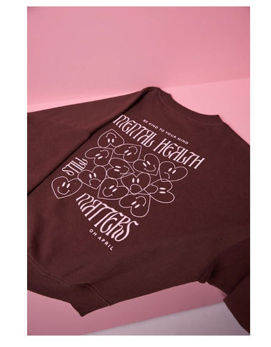 Regular Sweater Mental Health Brown von OH APRIL – brauner Pullover aus 100 % Baumwolle mit Mental Health Still Matters Print und OH APRIL Stickerei auf der Brust, locker geschnitten und leicht verkürzt.