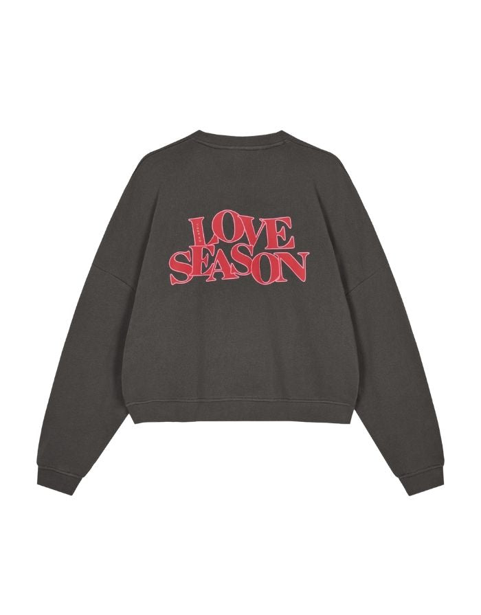  Light Love Season Sweater von OH APRIL in Graphite mit großem Love-Season-Print auf dem Rücken und kleinem Logo auf der Brust, entspannte Passform, leicht verkürzt, aus weichem Baumwollmix mit klassischem Rundhalsausschnitt.