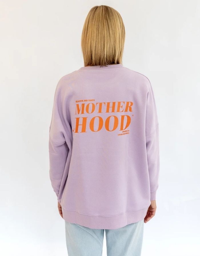Liliput Motherhood Oversize Sweatshirt für Damen mit kleinem orangefarbenem Herz auf der Vorderseite und großem Motherhood-Schriftzug auf dem Rücken, getragen.