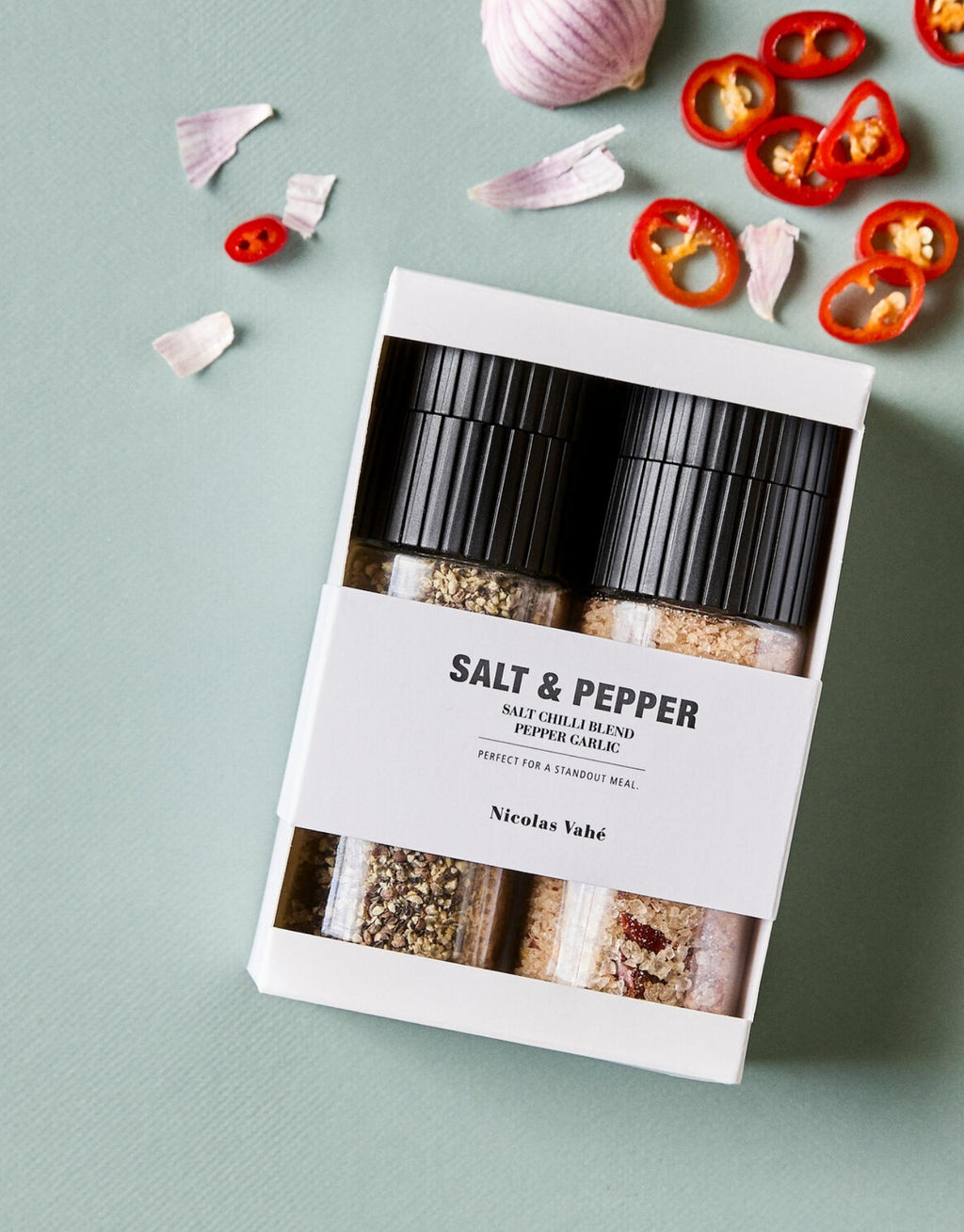 Geschenkbox Chili Blend &amp; Pfeffer Knoblauch von Nicolas Vahé mit zwei aromatischen Gewürzmischungen aus Chilisalz und schwarzem Pfeffer mit Knoblauch mit Verpackung neben Chili und Knoblauch