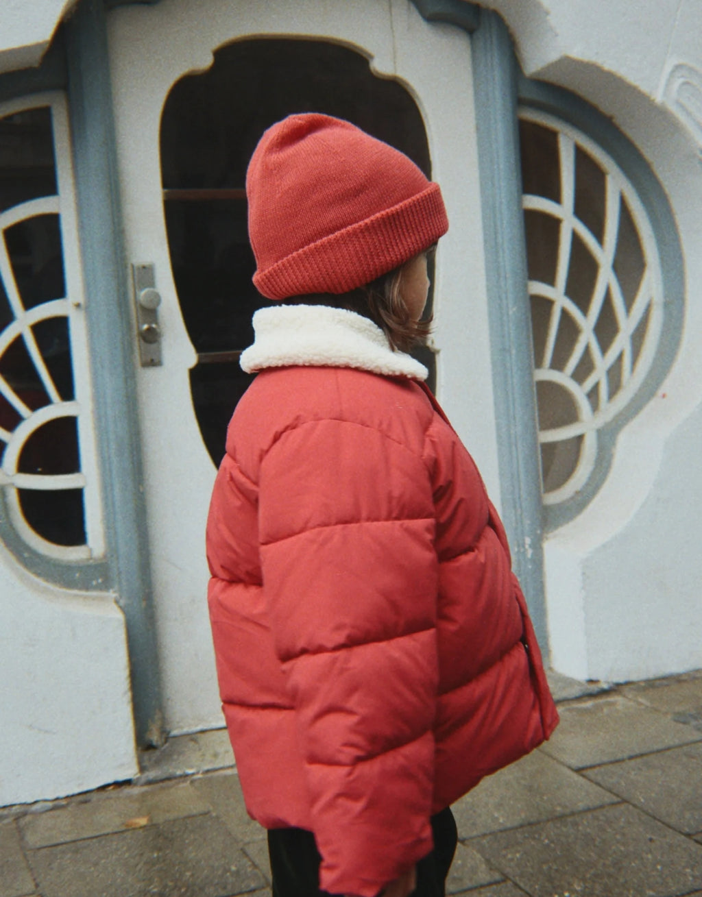 Avely Beanie von Konges Sløjd in der Farbe Cardinal aus weicher Bio-Baumwolle mit klassischer Rippstrickstruktur und verstellbarem Umschlag, am Model von der Seite.