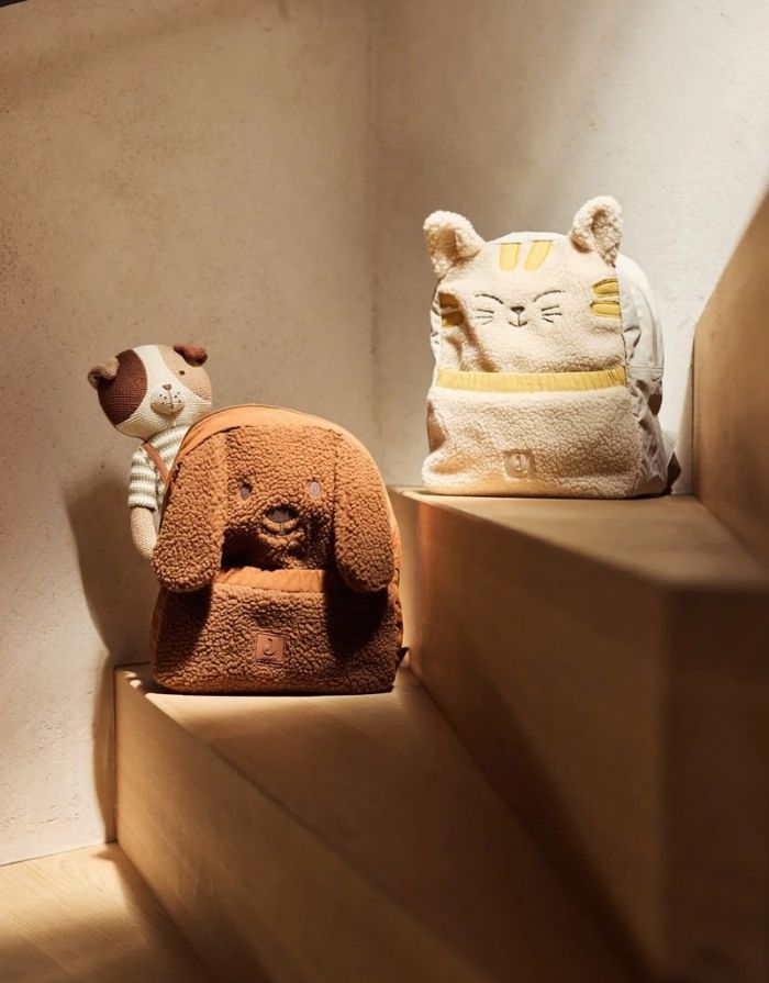 Jollein Rucksack Charlie Cat mit Teddy-Stoff, Katzenohren und verstellbaren Schultergurten für Kinder auf einer Treppe mit einem weitern Rucksack 