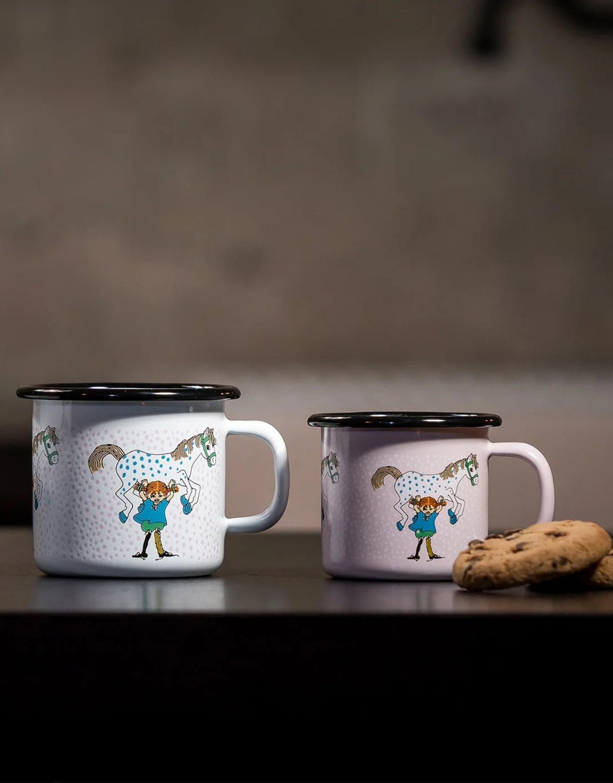 Pippi Langstrumpf Emaille-Becher von Muurla mit Pippi und ihrem Pferd Kleiner Onkel, dekorativer Trinkbecher aus emailliertem Stahl mit Henkel und 250 ml Fassungsvermögen neben Keksen