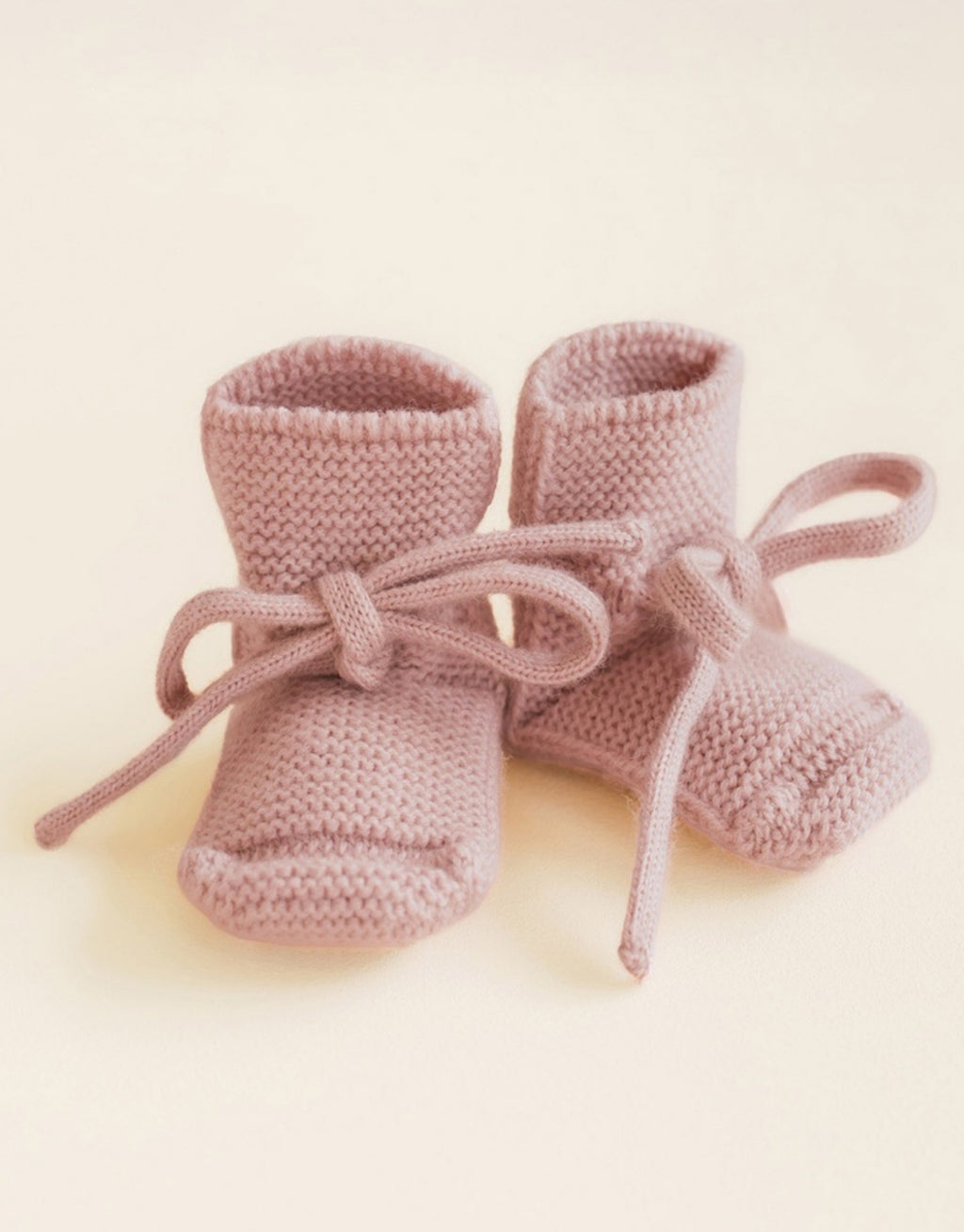 Booties von Heid aus Merinowolle in der Farbe Powder für Babys im Alter von 0-9 Monaten auf gelbem Hintergrund