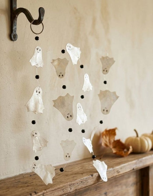 Weiße Halloween Girlande Ghostie von BOLTZE mit handgefertigten Gespenstern aus Capiz, 180 cm lang, vor einer Wand.