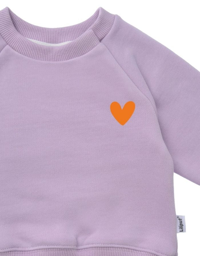 Liliput Childhood Oversize Sweatshirt für Kinder in Flieder mit kleinem Herz auf der Vorderseite und großem typografischem Rückenprint, Nahaufnahme.