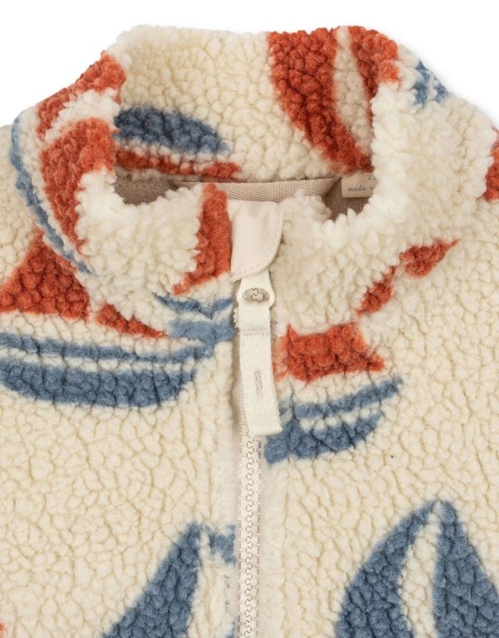 Die Teddyjacke Jody Ahoy von Konges Sløjd ist ein kuscheliger Begleiter für kalte Tage und aktive Abenteuer im Freien. Das weiche Teddy-Material aus recyceltem Polyester hält angenehm warm, während das innenliegende Fleece für zusätzlichen Komfort sorgt. Mit ihrem hohen Kragen schützt die Jacke zuverlässig vor Wind, und die elastischen Ärmelbündchen sorgen für einen guten Sitz. Der durchgehende Frontreißverschluss macht das An- und Ausziehen besonders einfach – ideal für den Alltag mit Kindern. Das Ahoy-Des
