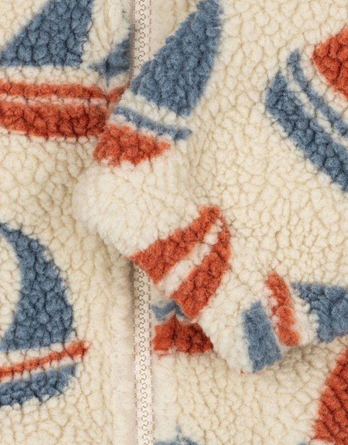 Die Teddyjacke Jody Ahoy von Konges Sløjd ist ein kuscheliger Begleiter für kalte Tage und aktive Abenteuer im Freien. Das weiche Teddy-Material aus recyceltem Polyester hält angenehm warm, während das innenliegende Fleece für zusätzlichen Komfort sorgt. Mit ihrem hohen Kragen schützt die Jacke zuverlässig vor Wind, und die elastischen Ärmelbündchen sorgen für einen guten Sitz. Der durchgehende Frontreißverschluss macht das An- und Ausziehen besonders einfach – ideal für den Alltag mit Kindern. Das Ahoy-Des