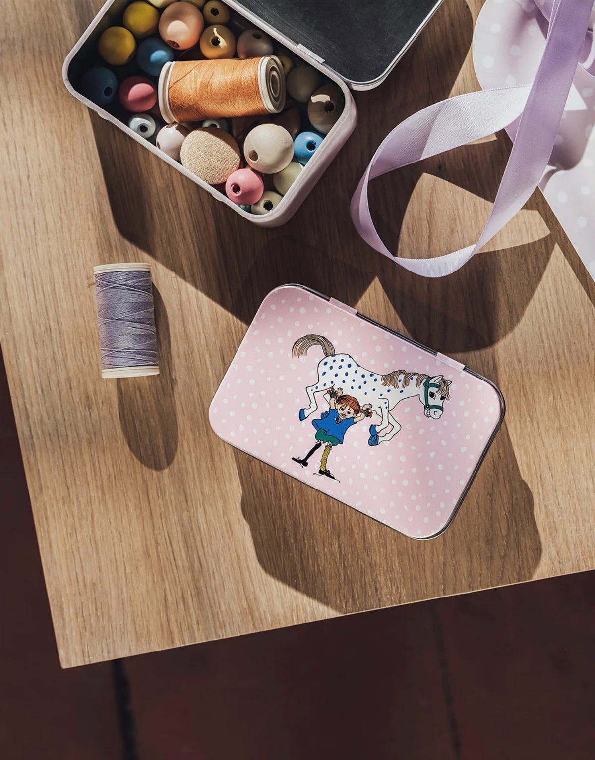 Pippi Langstrumpf Blechdose von Muurla mit Pippi und ihrem Pferd Kleiner Onkel, kleine dekorative Metalldose mit Deckel und nostalgischem Motiv, 10 x 6,5 cm auf einem Tisch neben Garn
