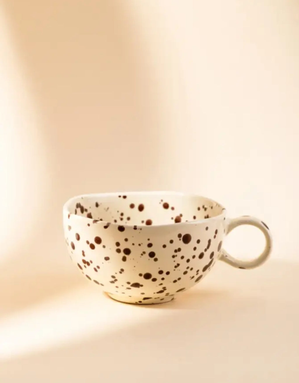 Becher Kenki von HOMLA in Ecru, 300 ml großer Keramikbecher aus Steingut mit unregelmäßigen schwarzen Sprenkeln, abgerundeter Form und individueller reaktiver Glasur.