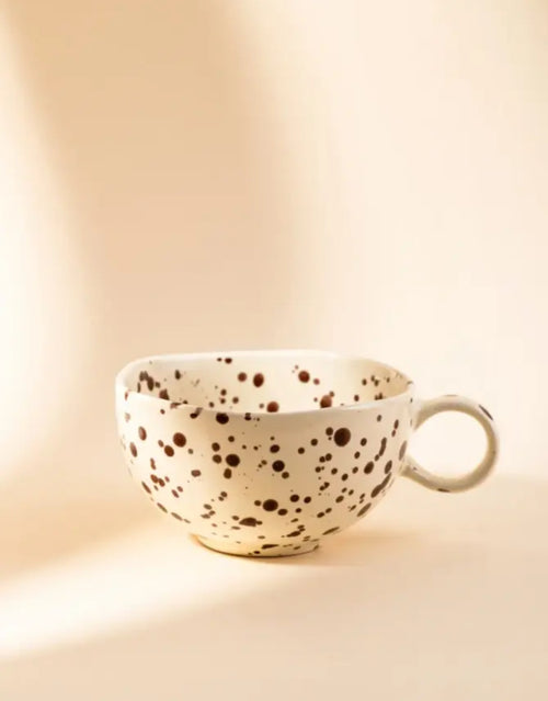 Becher Kenki von HOMLA in Ecru, 300 ml großer Keramikbecher aus Steingut mit unregelmäßigen schwarzen Sprenkeln, abgerundeter Form und individueller reaktiver Glasur.