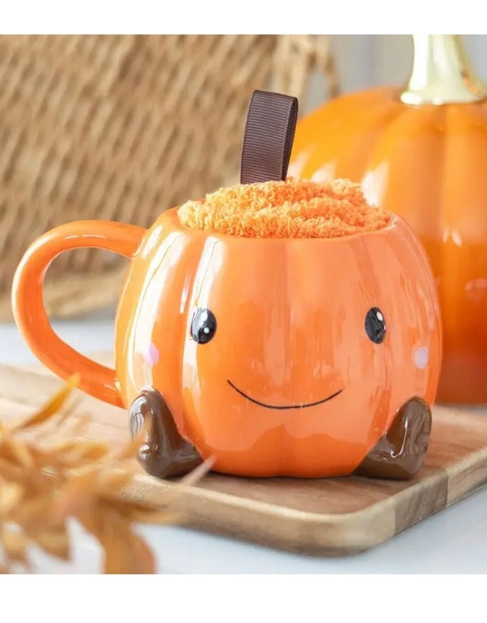 Halloween Geschenkset von Something Different mit orangefarbener Kürbistasse mit Gesicht und passenden flauschigen Socken auf einem Brett