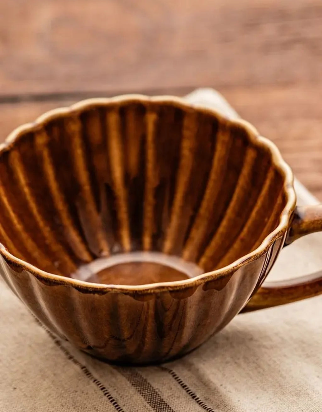 Tasse Melida von HOMLA in Bernstein, 300 ml große Keramiktasse aus Steingut mit geriffelter Oberfläche, gewelltem Rand und individueller reaktiver Glasur in warmen Bernsteintönen.