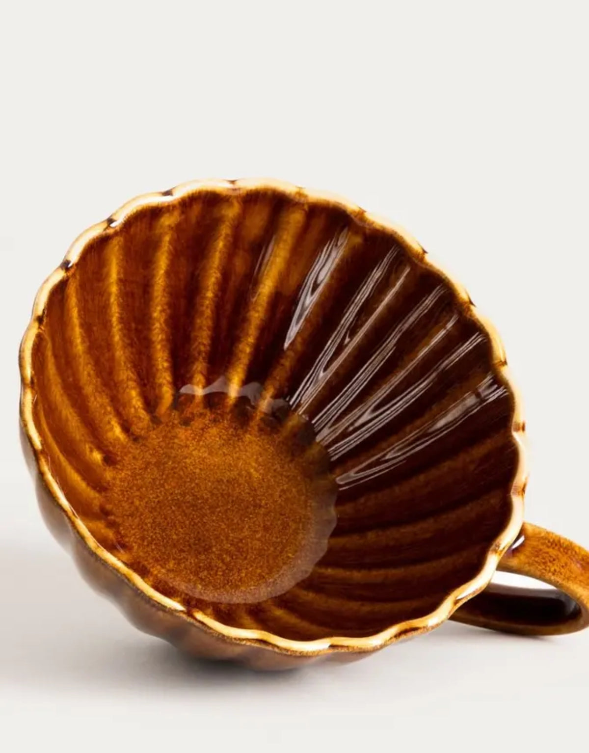 Tasse Melida von HOMLA in Bernstein, 300 ml große Keramiktasse aus Steingut mit geriffelter Oberfläche, gewelltem Rand und individueller reaktiver Glasur in warmen Bernsteintönen.