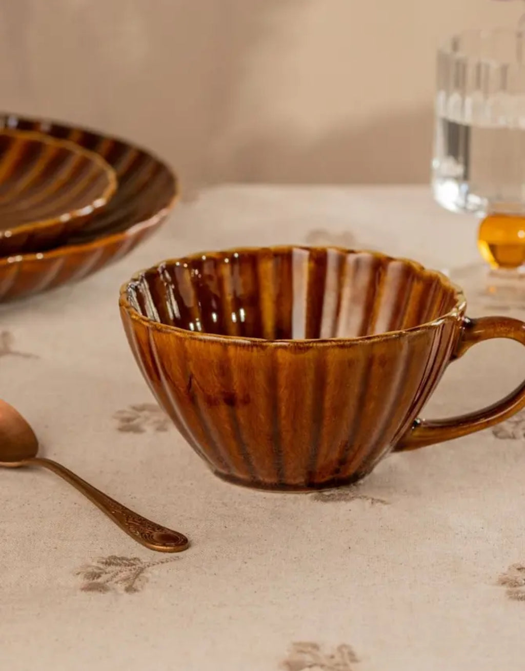 Tasse Melida von HOMLA in Bernstein, 300 ml große Keramiktasse aus Steingut mit geriffelter Oberfläche, gewelltem Rand und individueller reaktiver Glasur in warmen Bernsteintönen.