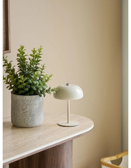 Portable Tischlampe Margate von House Nordic in Beige aus Metall mit fest verbauter LED und wiederaufladbarem Akku neben einer Pflanze