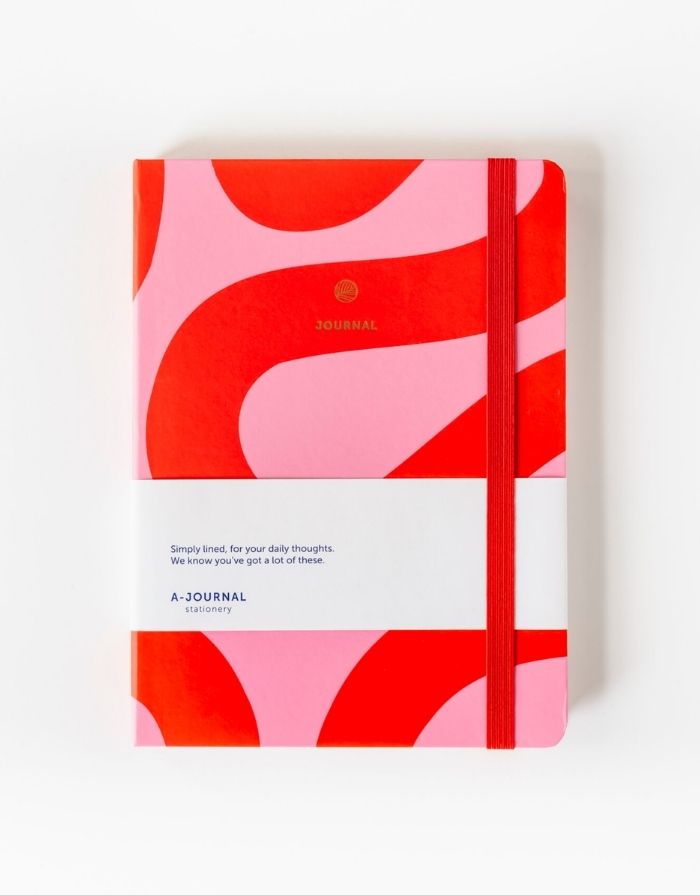 Notizbuch von A Journal in Rosa und Rot von vorne mit beige Hintergrund