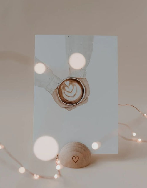 Postkarte in Weiß von Eulenschnitt in Kartenständer mit Händen die einen Kaffee halten