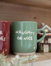 Laden Sie das Bild in den Galerie-Viewer, Grüner Steingutbecher mit weißem Schriftzug „Naughty or Nice“ von Det Gamle Apotek, festlicher Kaffeebecher.
