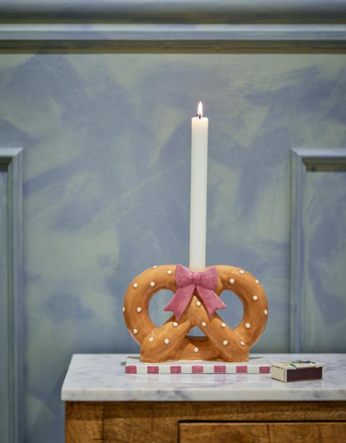 Brauner Pretzie Kerzenhalter von Bloomingville aus handbemalter Keramik in Brezelform mit weißen Punkten und rosa weiß gestreiftem Sockel.