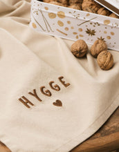Laden Sie das Bild in den Galerie-Viewer, Leinenfarbenes Geschirrtuch mit „Hygge“-Schriftzug von Ib Laursen, Größe 50x70 cm.
