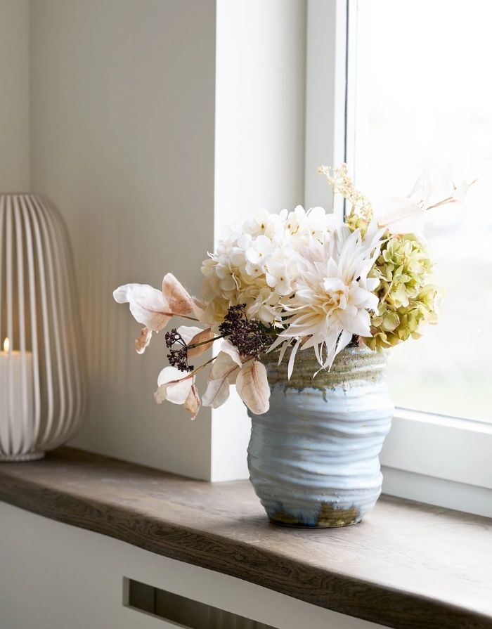 Hellblaue Keramikvase von House Nordic mit bauchiger Form und dekorativer Oberfläche auf der Fensterbank mit Blumen
