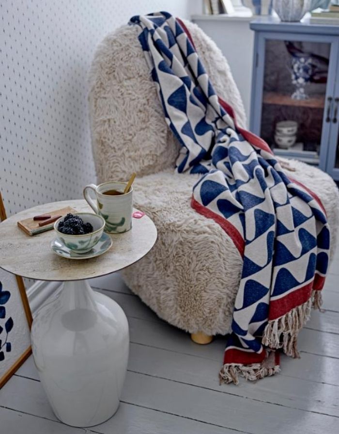 Bunte Decke Rimme von Creative Collection by Bloomingville mit blauem Wellenmuster, roten und beigen Akzenten und Fransen, 160 × 130 cm, über einem Sessel.