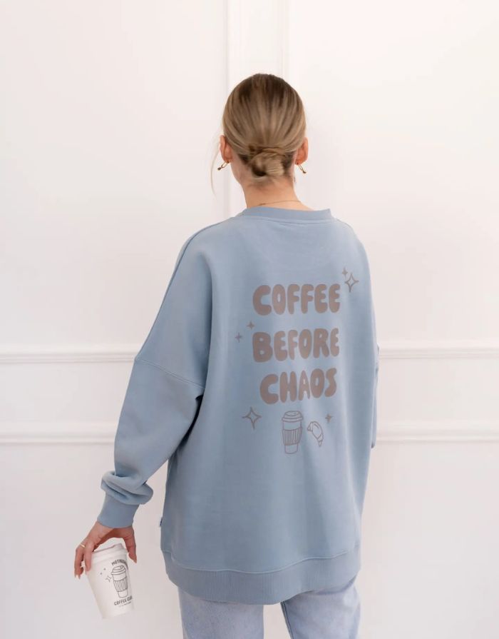 Fliederfarbenes Oversized Sweatshirt von Liliput mit „6am“-Print auf der Brust und großem Rückenschriftzug „Coffee before the Chaos evolves“ – gemütlich und stylisch für den Eltern-Alltag.
