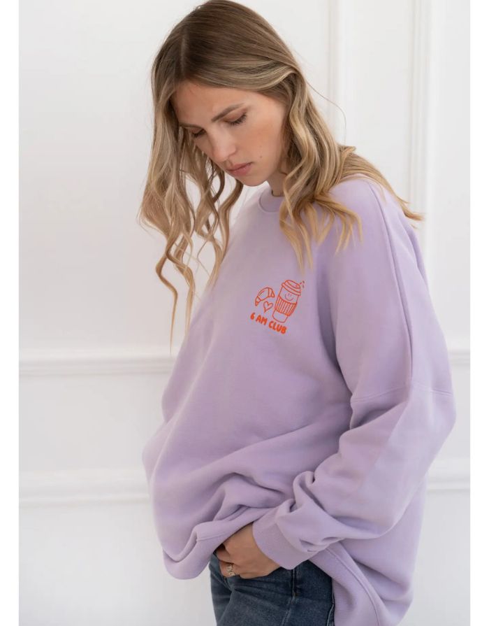 Fliederfarbenes Oversized Sweatshirt von Liliput mit „6am“-Print auf der Brust und großem Rückenschriftzug „Coffee before the Chaos evolves“ – gemütlich und stylisch für den Eltern-Alltag.