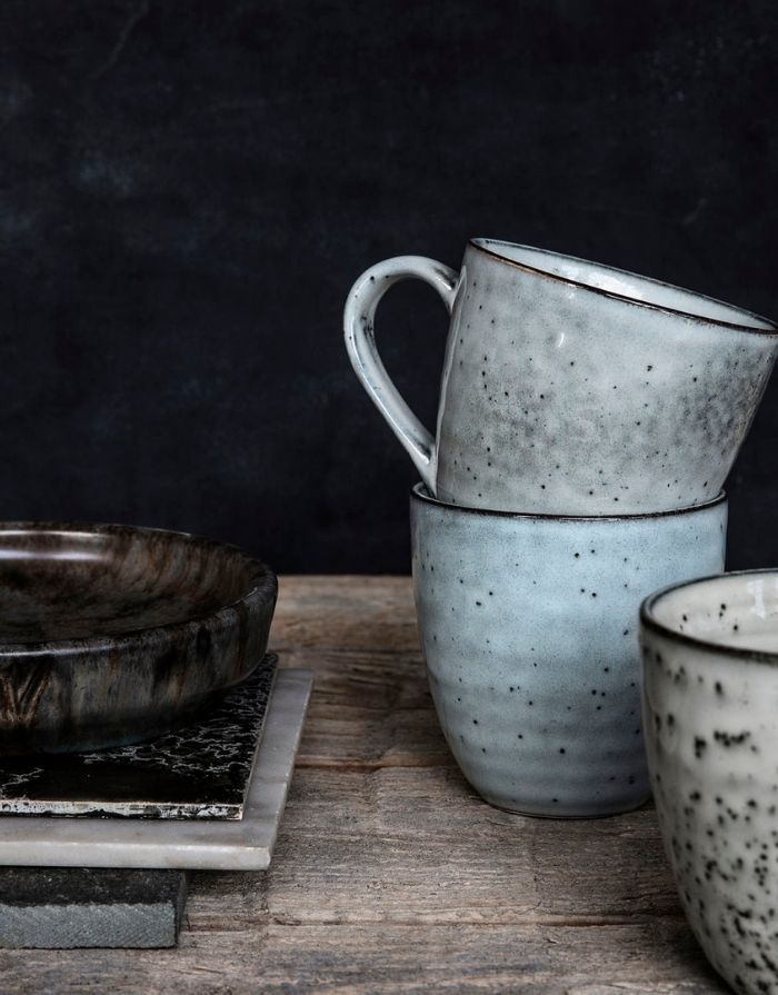 Handgefertigter Steinzeugbecher Rustic von House Doctor in Grau und Blau mit gesprenkelter Glasur und skandinavischem Design auf Holzplatte mit weiteren Bechern